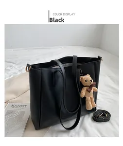 Detail of black PU leather tote bag with a beige knitted bear charm on a white fabric