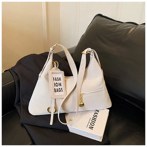 Détail du sac hobo blanc avec ferrures dorées posé sur un canapé en cuir noir élégant