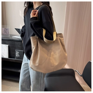 Side view of a large beige canvas tote bag with wide straps shown on a model