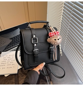 Detail of black pebbled leather mini backpack featuring a plush bear charm and handle