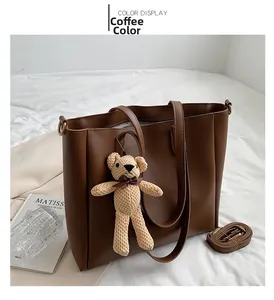 Detail of coffee brown tote bag with bear charm and adjustable strap on white bedding