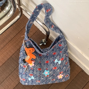 Dettaglio della borsa tote in denim patchwork con fiori, fiocchi e un ciondolo a cavallo