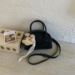 Close-up of black retro bowling bag with plush bear charm and adjustable strap