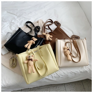 Top-down view of four colorful PU leather tote bags with cute bear charms on white fabric