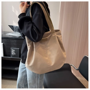Detail of oatmeal canvas tote bag showing wide nylon straps and embossed brand logo