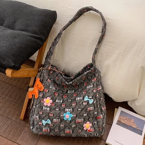 Dettaglio della borsa tote in denim grigio con applicazioni floreali e ciondolo