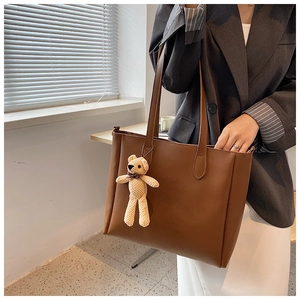 Close-up of a brown leather tote bag featuring a cute teddy bear pendant for commuting