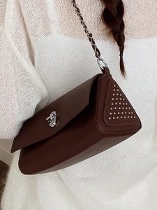 Deep brown crossbody bag with silver buckle and rivets shown on a stylish model