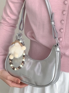 Silberne Metallic-Hobo-Tasche mit Plüschanhänger und Perlenkette an einem Modell
