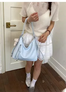 Detail of light blue faux leather tote bag with plush bear charm and multiple straps