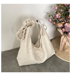 Detailed view of cream canvas tote bag with silver star patterns and ruched shoulder strap