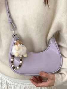 Schicke helllila Halbmond-Tasche mit Plüsch-Anhänger an einem stylischen Model