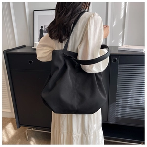 Side view of a large black minimalist tote bag worn by a model in a modern room