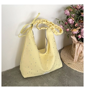 Detail shot of yellow canvas tote bag featuring silver stars and ruched ribbon strap