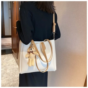 Detailed view of beige tote bag with brown straps and woven bear charm on a model