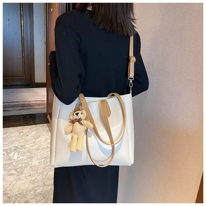 Detailed view of white leather tote bag with brown straps and cute teddy bear charm