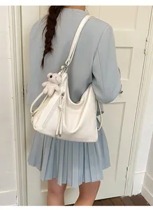 Detail of a creamy white Hobo bag with side zipper tassels and a cute teddy bear charm