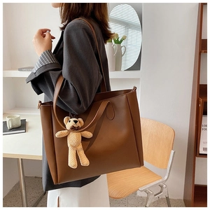 Detail of large dark brown leather tote bag with stylish knit bear charm accessory