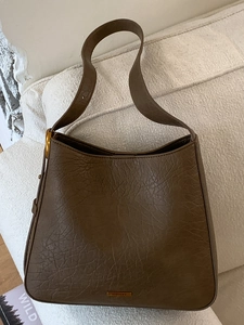 Vintage dark brown lychee leather tote bag with gold logo on a white sofa