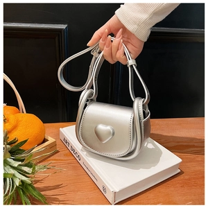 Detail of silver mini bag with 3D heart decor held over a book on wooden background