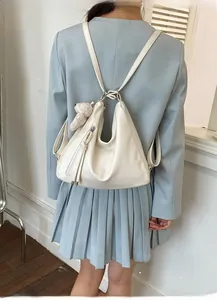 Detail view of cream white leather hobo backpack with plush bear and tassel on blue suit