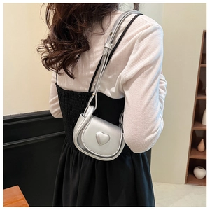 Close-up of a mini silver heart crossbody bag worn by a model in a fashion outfit