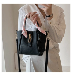 Dettaglio borsa a secchiello nera a grana con chiusura dorata e foulard decorativo