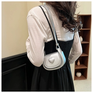 Mini silver heart saddle bag shown on a model in a minimalist indoor setting