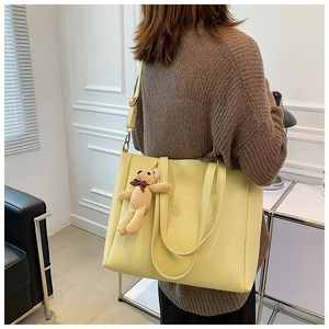 Detail of large yellow faux leather tote bag with cute beige teddy bear plush charm