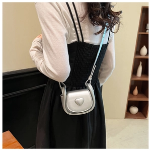 Detail shot of a silver metallic heart-shaped mini crossbody bag worn over the shoulder
