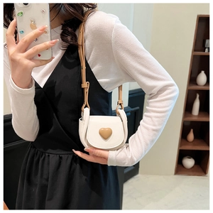 Mini white crossbody bag with brown heart detail shown worn by a model in a cozy setting
