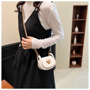 Detailed view of mini white crossbody bag with brown heart motif on girl's outfit