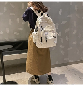 Detail of white nylon multi-pocket backpack with cute bear pendant and badges for school
