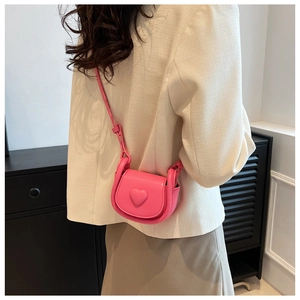 Girl's pink mini heart crossbody bag worn over a cream outfit in a casual indoor setting