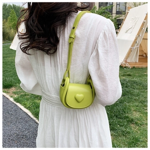 Girl's green heart-shaped crossbody bag shown on a white dress in a park outdoor setting