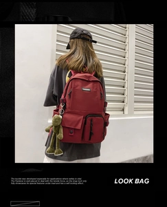 Close-up of a burgundy nylon school backpack with a cute frog pendant and multi-pocket design
