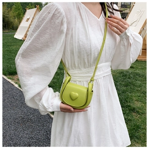 Detailed view of mini green leather crossbody bag with 3D heart on outdoor grass