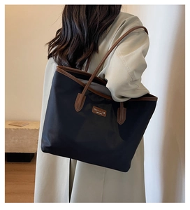Detail of a large contrast tote bag in black nylon and brown leather on model shoulder