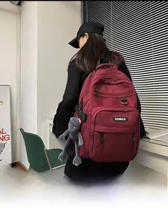 Deep red large capacity backpack with cute frog pendant worn by a model in a minimalist setting