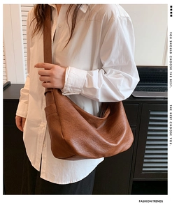 Brown leather crescent hobo bag with a wide strap shown on a model in a minimal interior