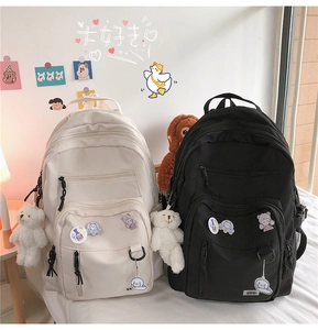 Detail view of large school backpacks with cute bear charms in black and beige canvas