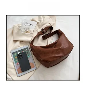 Detail of dark brown lychee texture leather hobo bag with adjustable strap on white blazer