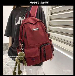 Detail view of red nylon backpack with multiple pockets and a green frog plush charm