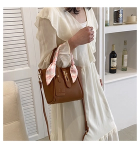 Dettaglio borsa a secchiello in pelle marrone con foulard rosa sul manico e chiusura oro