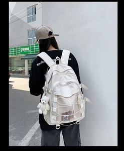 Detail of a creamy white nylon backpack featuring mesh pockets and a cute bear pendant charm