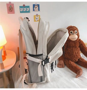 Detail of beige backpack with multi-layer zippers and side mesh pockets in bedroom