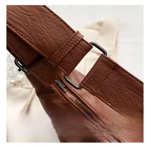 Detail of square dark gray metal hardware and neat stitching on brown leather shoulder bag