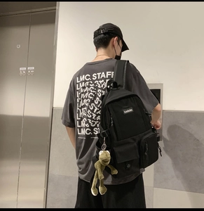 Side view of black nylon backpack with a green frog keychain and Ladata woven label
