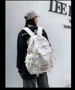 Close-up of beige canvas backpack with criss-cross rope detailing and plush bear charm