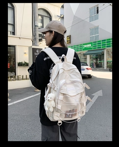 Outdoor shot of an off-white backpack with cross-rope detail and a cute bear charm